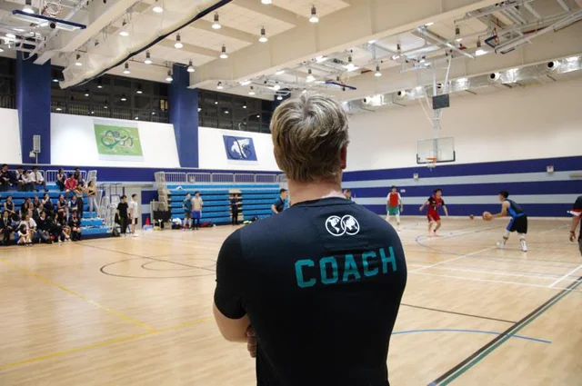 Jessiah watching a basketball game from the sideline in a coach shirt